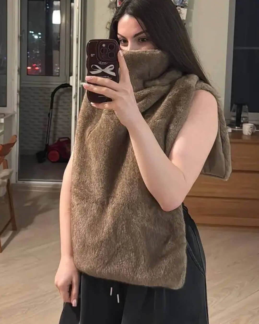 Person wearing a brown fuzzy vest taking a mirror selfie in a room.